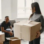 A smiling couple packing boxes in their living room, preparing for a smooth and organized move to a new home.