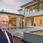 Portrait of Rex Tillerson in a formal suit with luxury homes in the background.