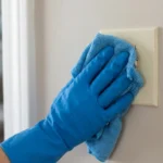 Close-up of cleaning gloved hands wiping a light switch, demonstrating a corrected mistake.